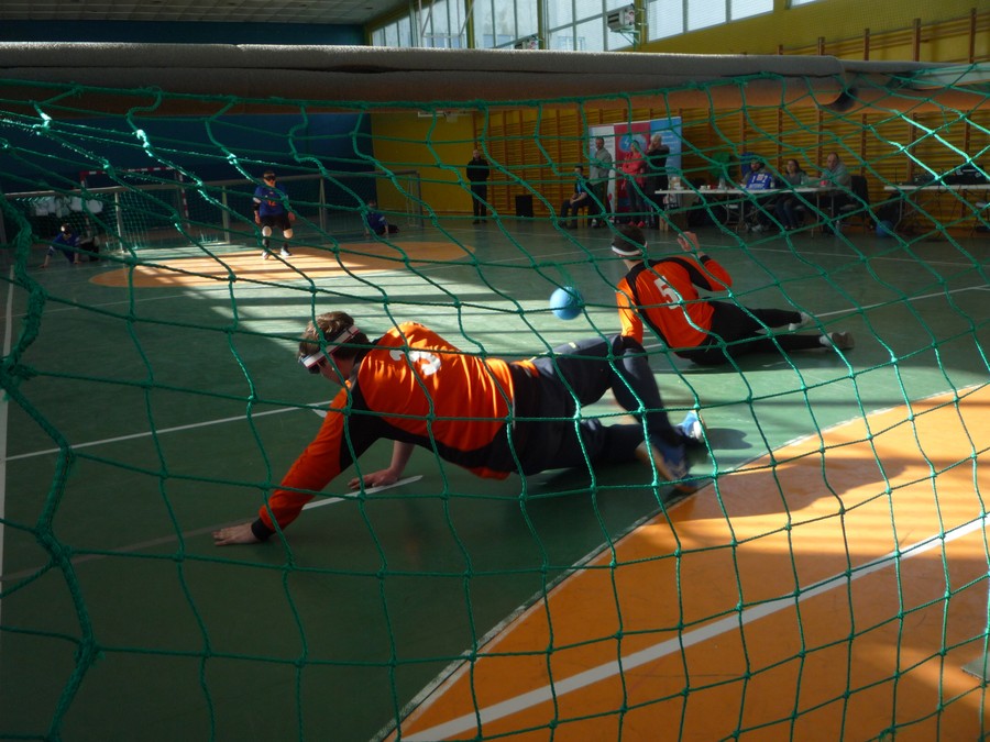 Mecz goalballa pomiędzy trzyosobowymi drużynami Bydgoszczy (pomarańczowe stroje) i Katowic (stroje niebieskie). Zdjęcie wykonane zza bramki bydgoskiej drużyny przedstawia graczy rywalizujących ze sobą podczas spotkania grupowego. Turniej odbywał się na terenie kompleksu sportowego CWZS Zawisza Bydgoszcz, fot. Jacek Knychała