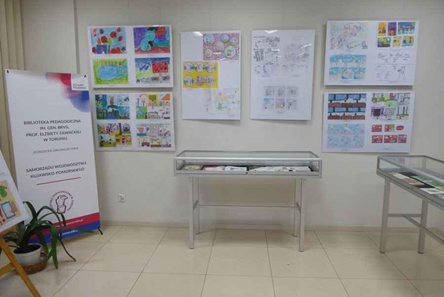 Na zdjęciu widoczna ściana sali wystawowej, na której wisi 6 antyram z pracami konkursowymi. Pod nimi stoją gabloty z książkami. Po lewej stronie stoi rollup Biblioteki, fot. Joanna Wosik