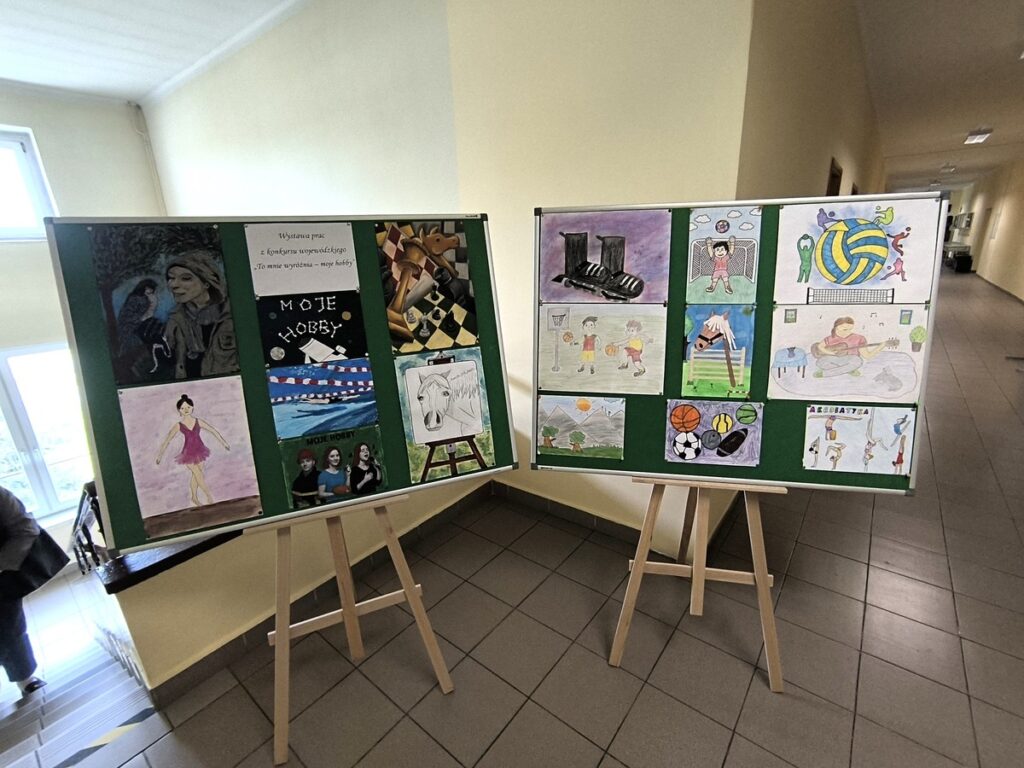 Dwie tablice na stelażach z przywieszonymi pracami konkursowymi.