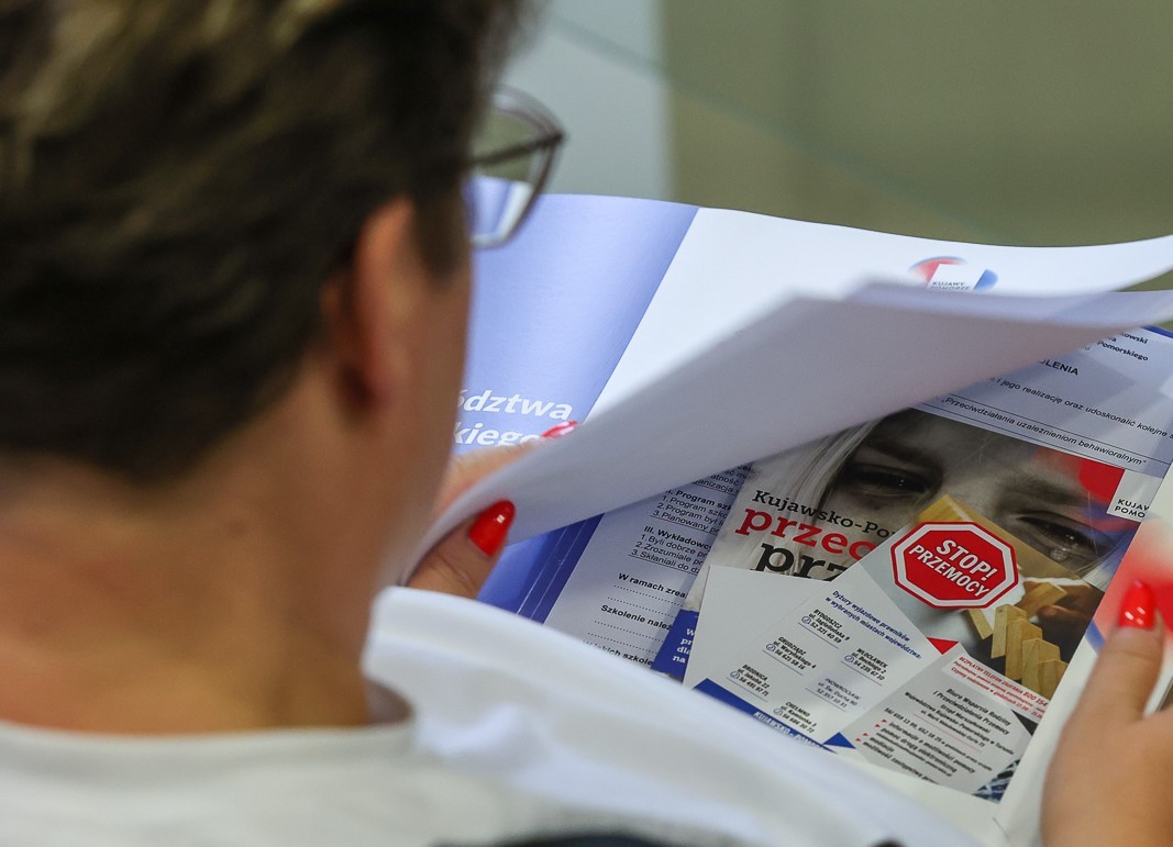 Pani patrząca na materiały informacyjne, ulotki o tematyce przemocy domowej