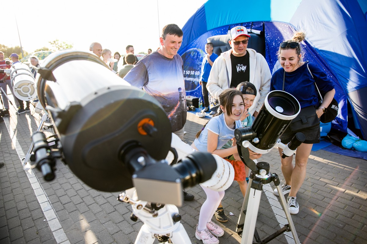 Na zdjęciu widać grupę ludzi stojących na zewnątrz i obserwujących coś przez teleskopy.