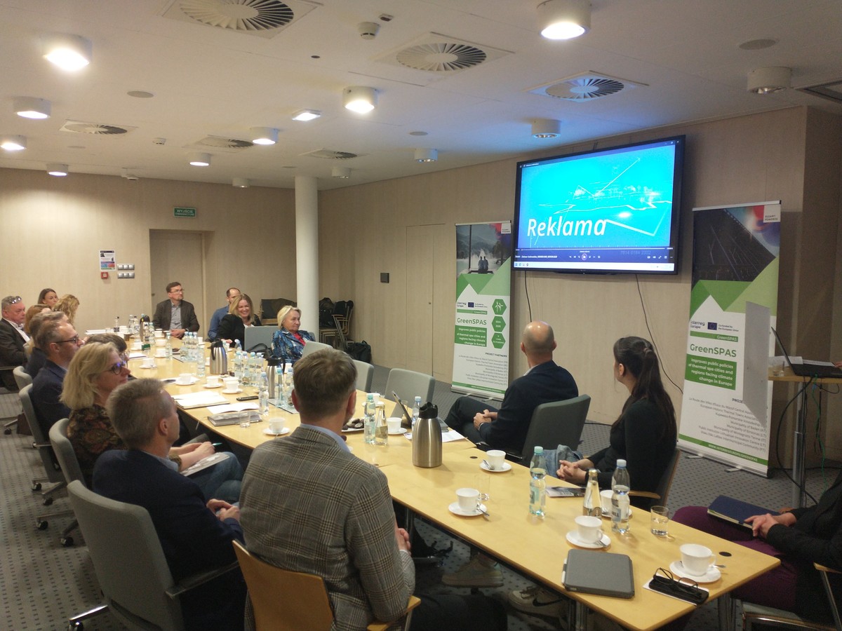 Uczestnicy spotkania skupieni na prezentacji siedząc przy stole