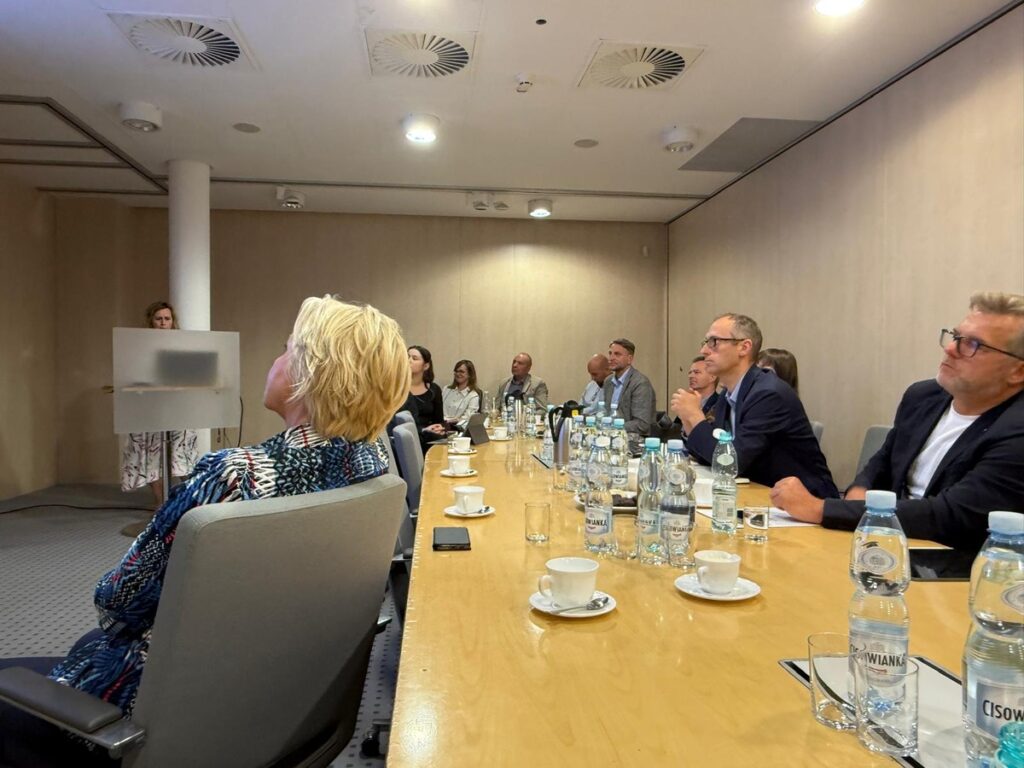 Uczestnicy spotkania skupieni na prezentacji siedząc przy stole